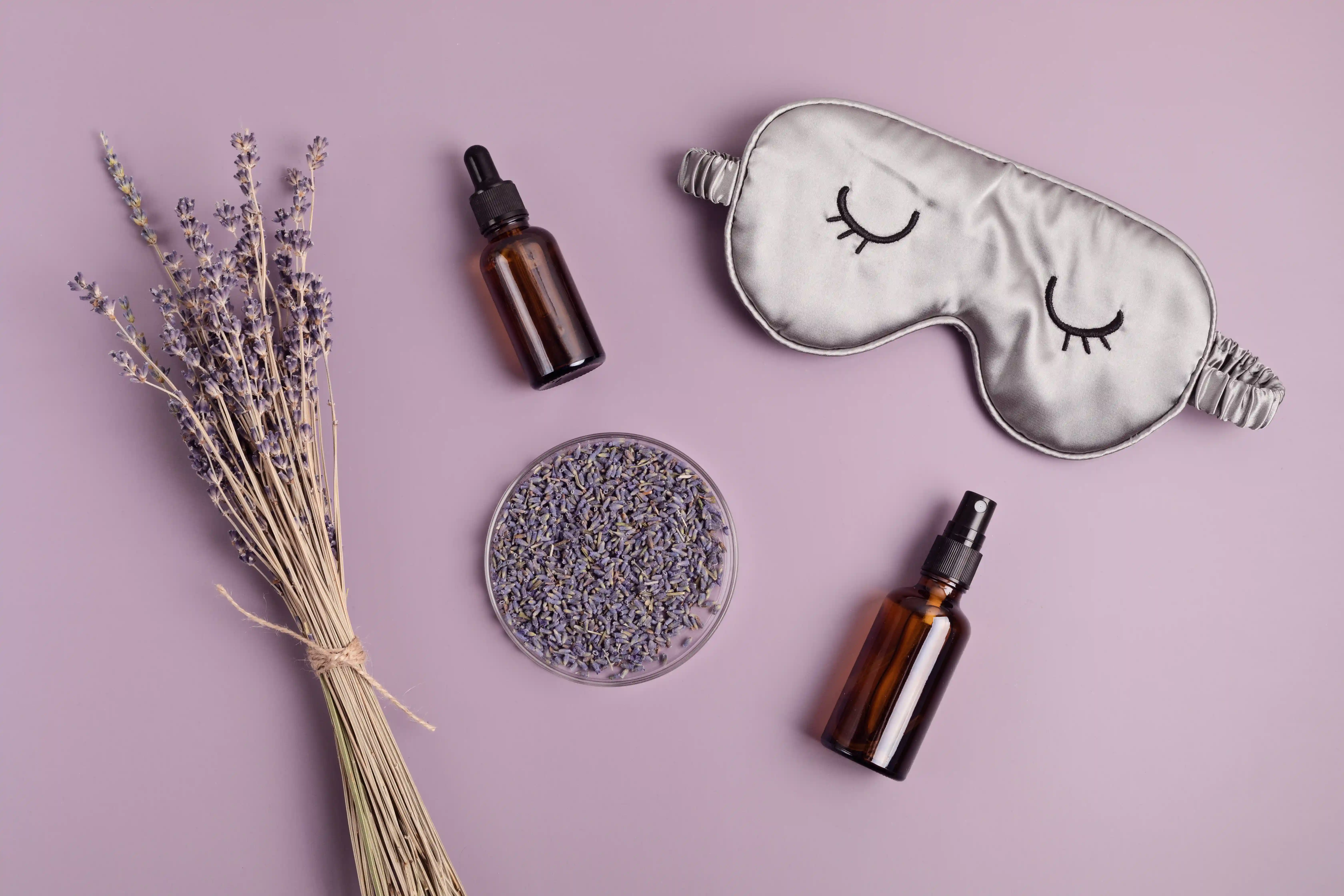 Lavender essential oil bottle and sleep mask on a purple background